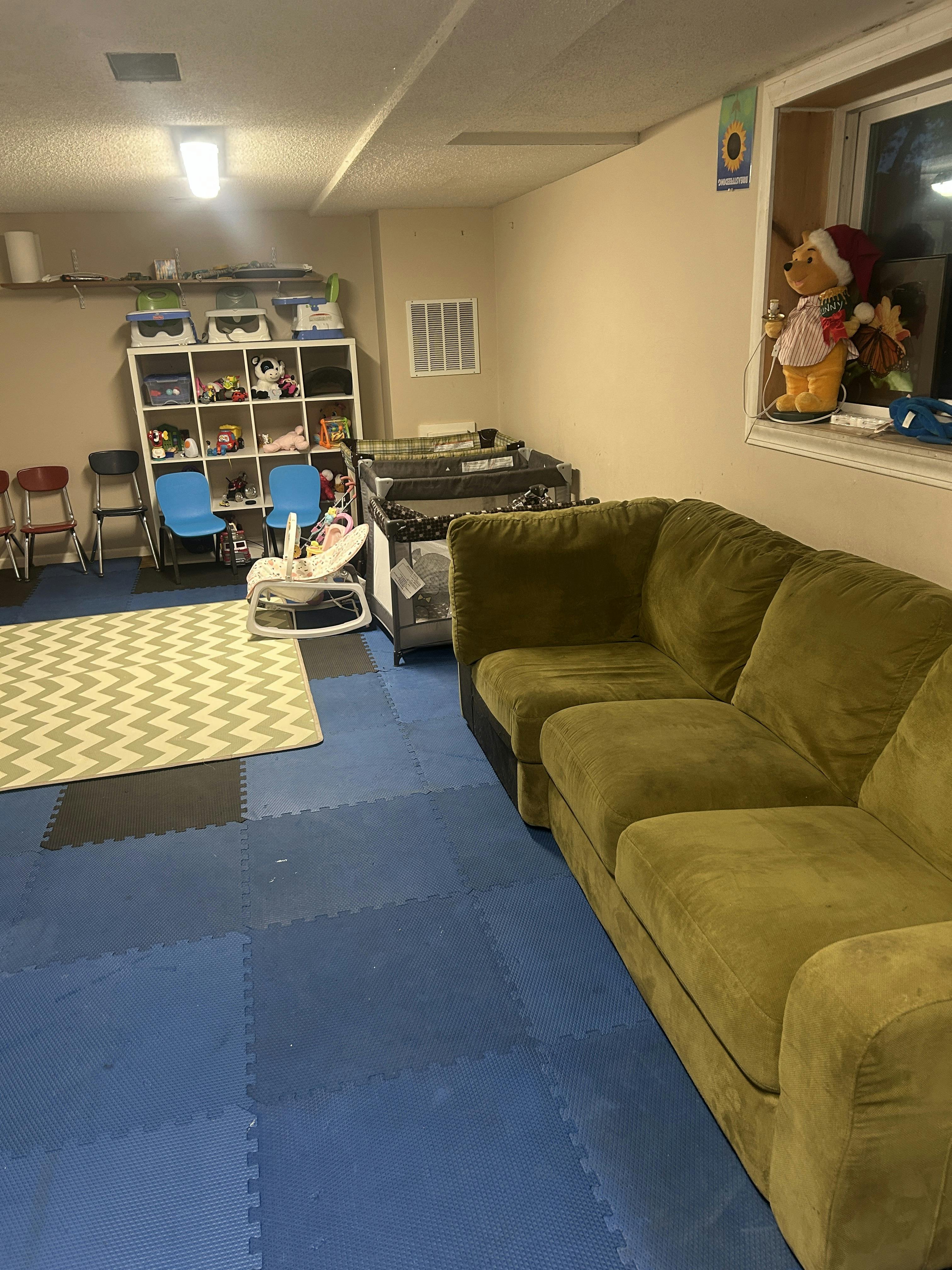Room with blue floor mats, a green sectional sofa, and a white storage shelf