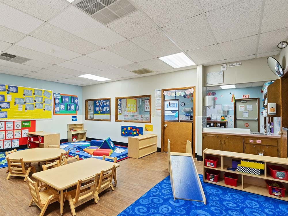 Classroom with small tables and chairs, play mats, and a slide