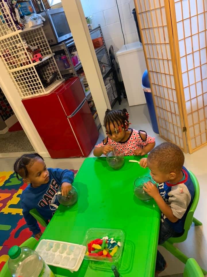 Three children sitting at a green table, stirring bowls
