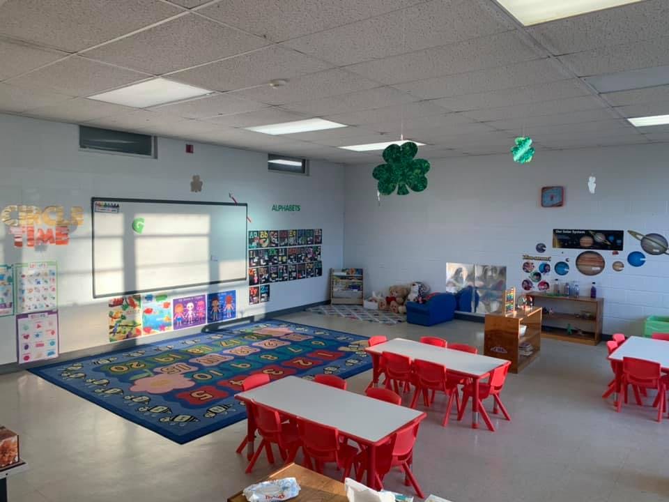 Empty classroom with small tables and chairs, a rug, and a whiteboard