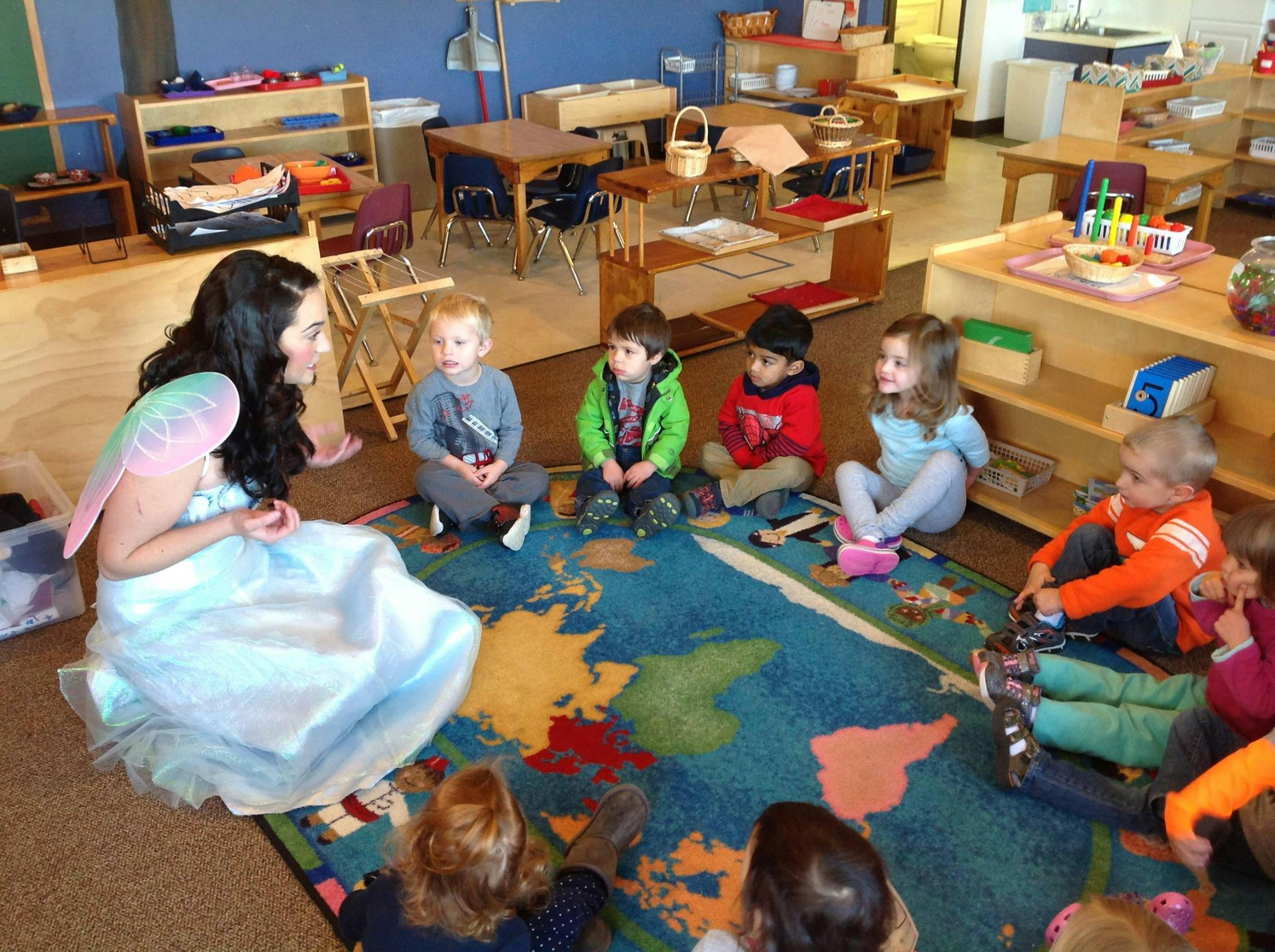Person in costume sitting on a rug with children
