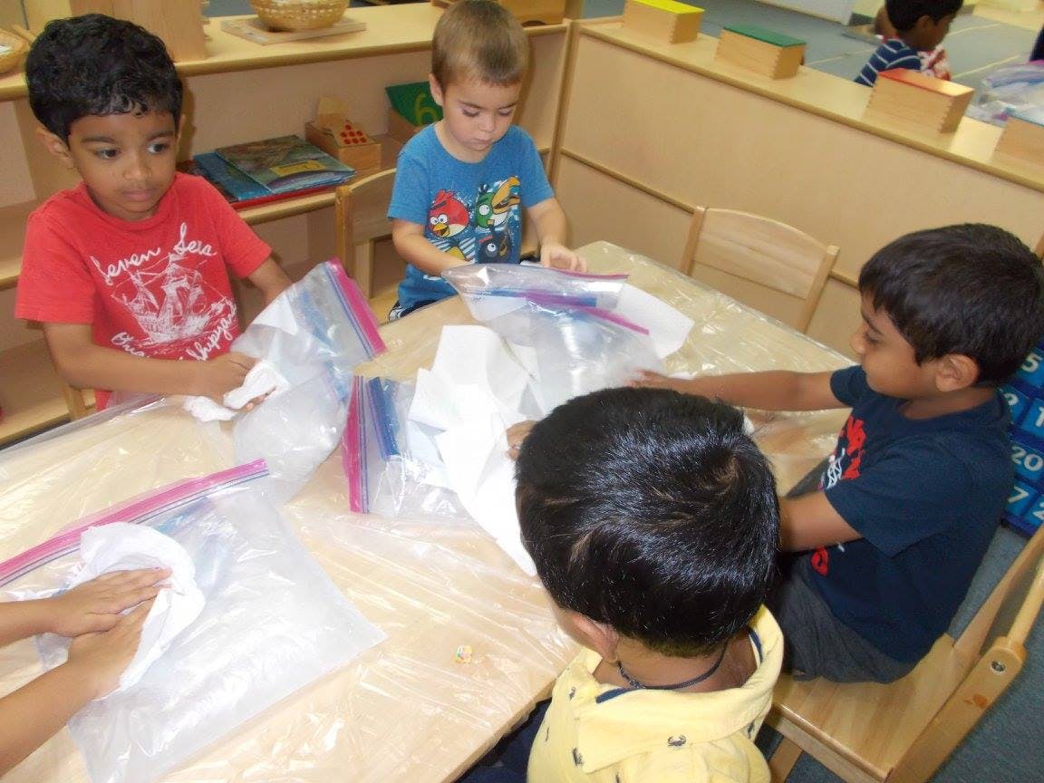 Four children sitting at a table with plastic bags