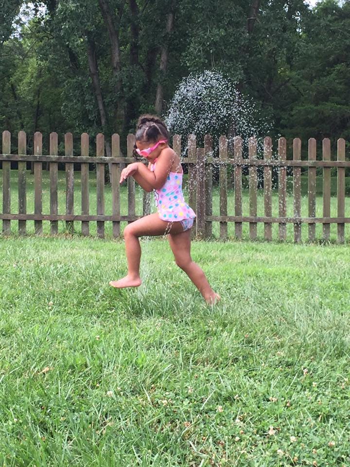 Child in swimsuit playing in sprinkler
