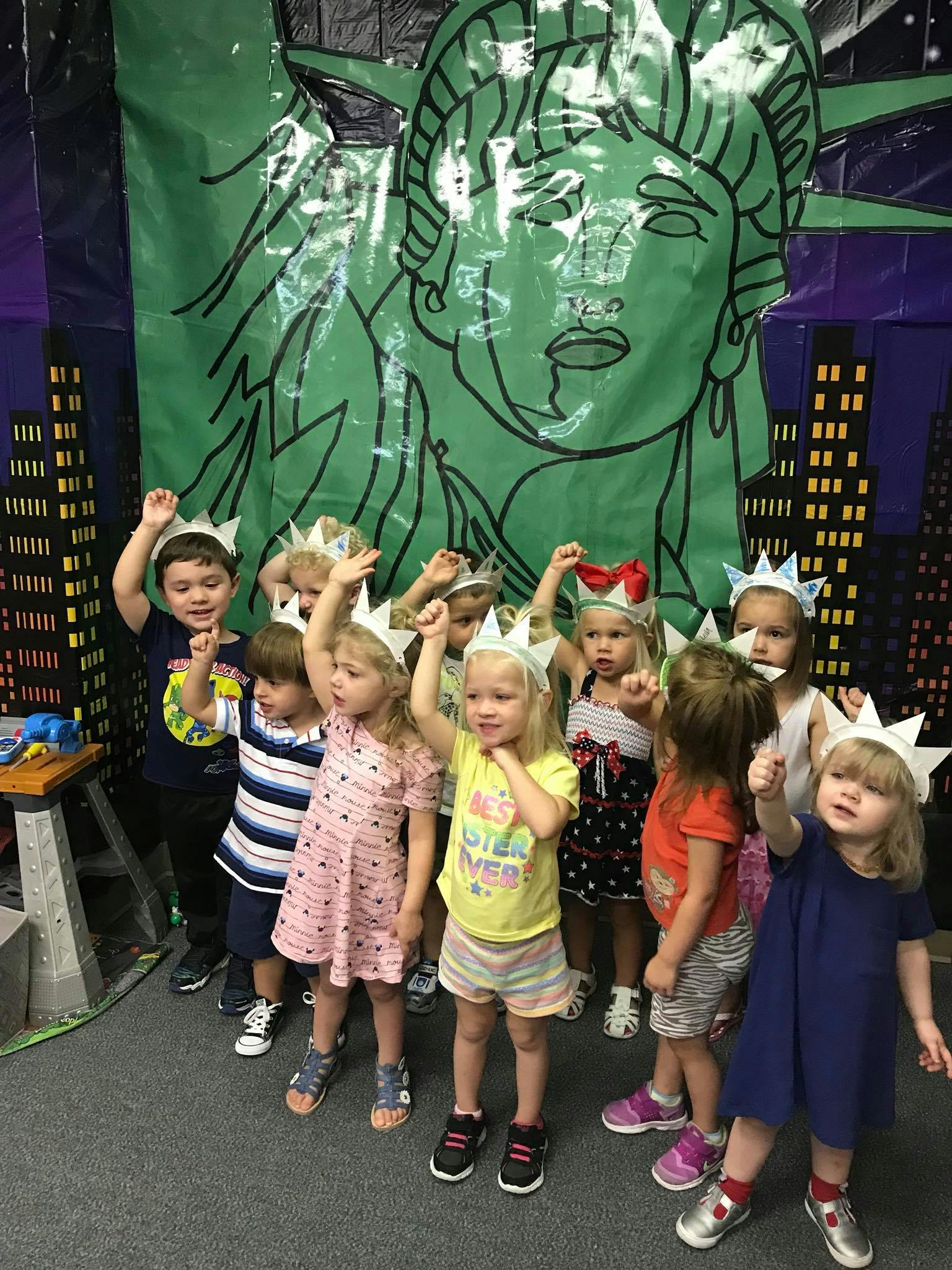 Group of children wearing paper crowns in front of a Statue of Liberty backdrop