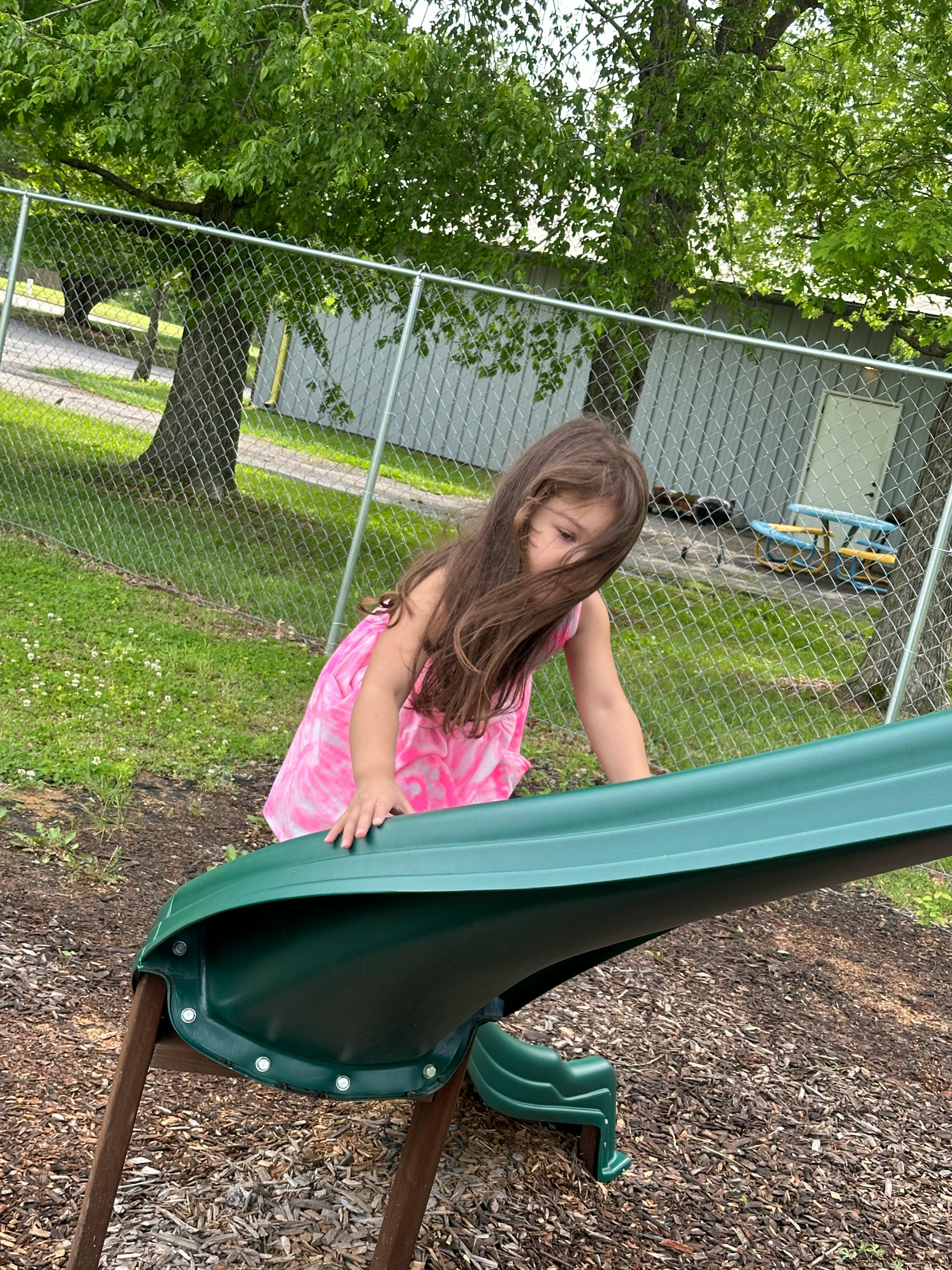 Child in a pink dress climbing onto a green slide