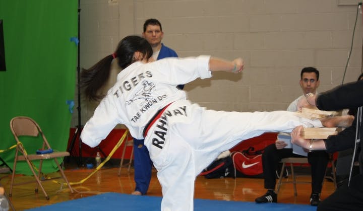 Person in white uniform performing a kick, breaking boards