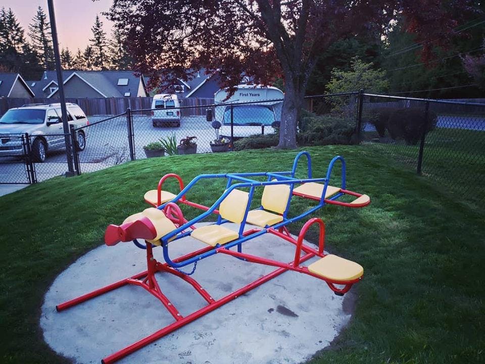 Red and blue playground seesaw with yellow seats on a concrete pad
