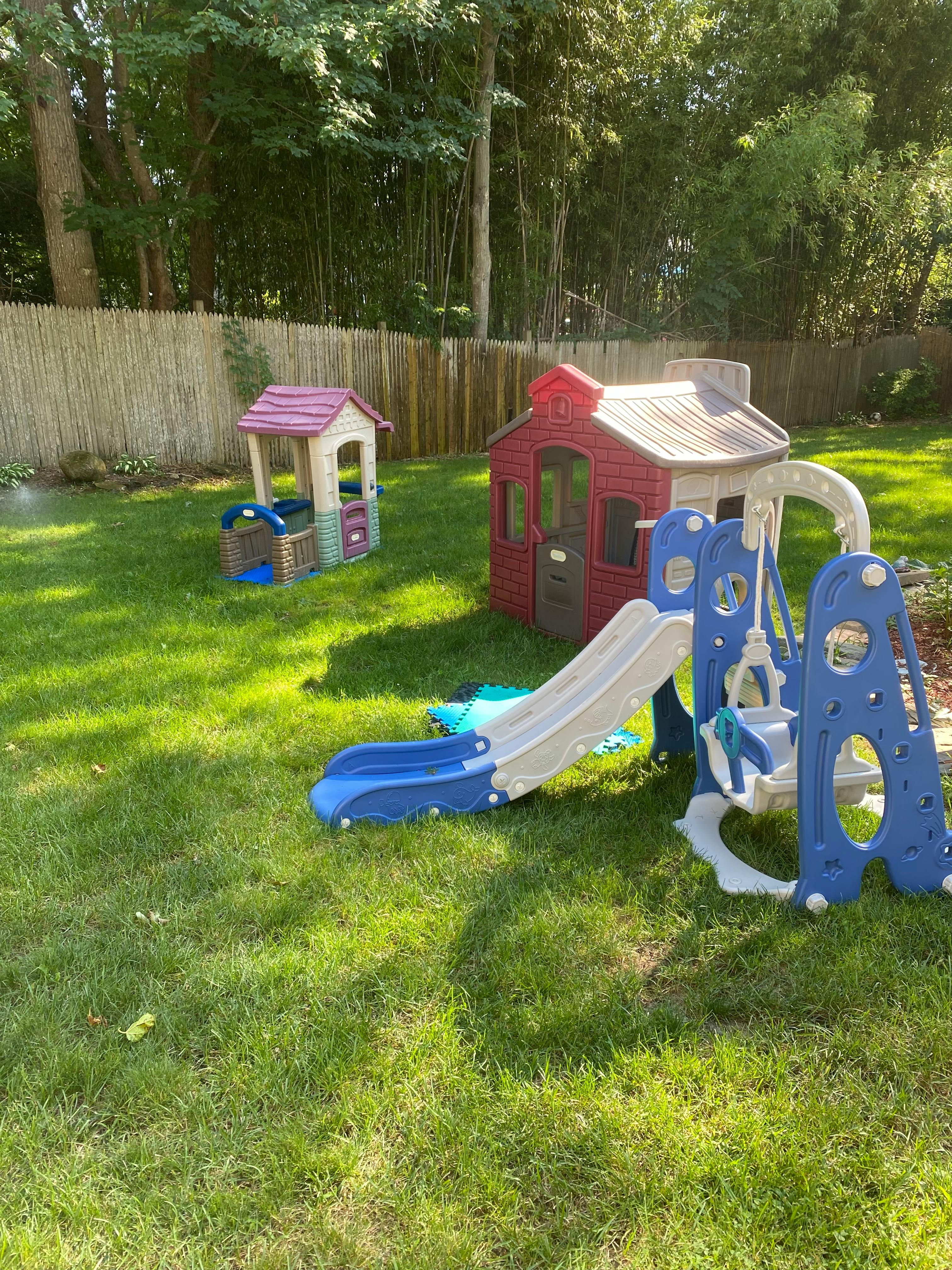 Playhouses and a swing set with a slide in a grassy yard