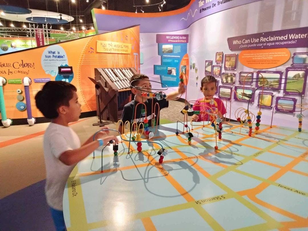Three children playing with a large bead maze table in a museum