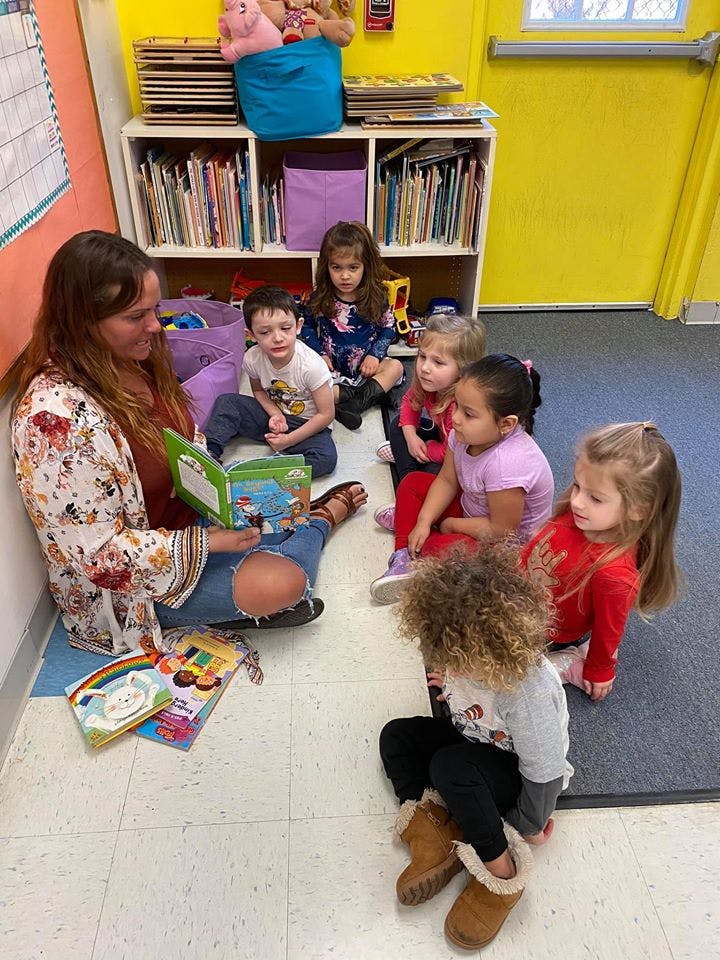 Person reading a book to a group of children in a classroom