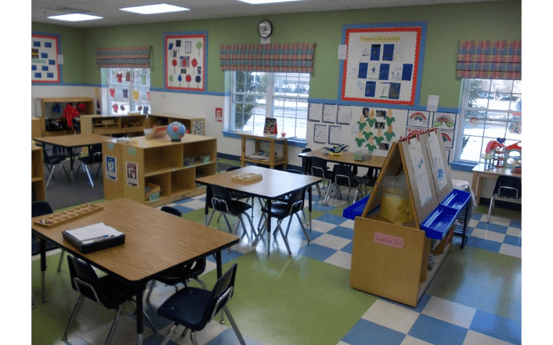 Classroom with tables, chairs, shelving units, and windows