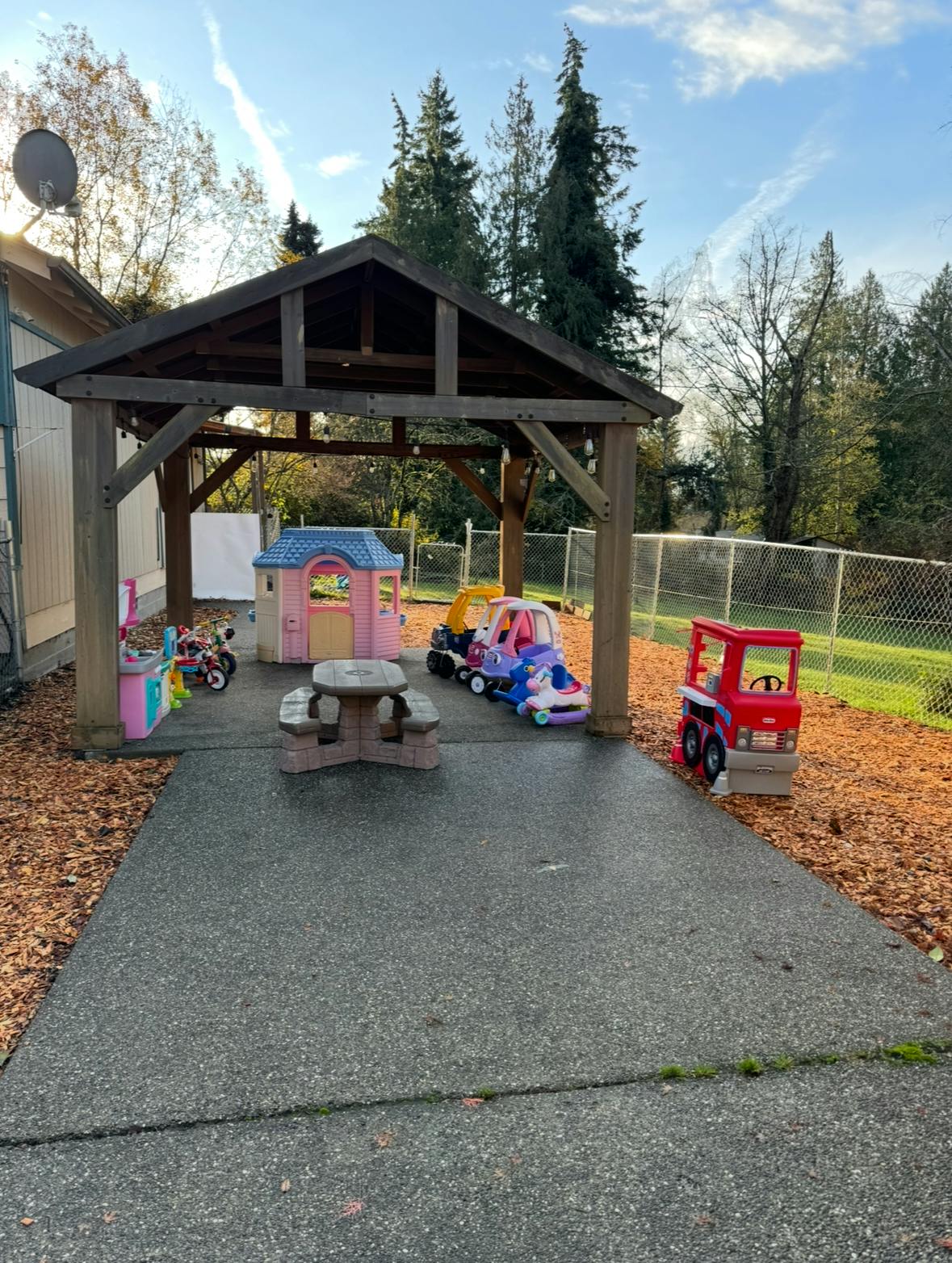 Outdoor play area with a wooden gazebo, toy cars, and a picnic table