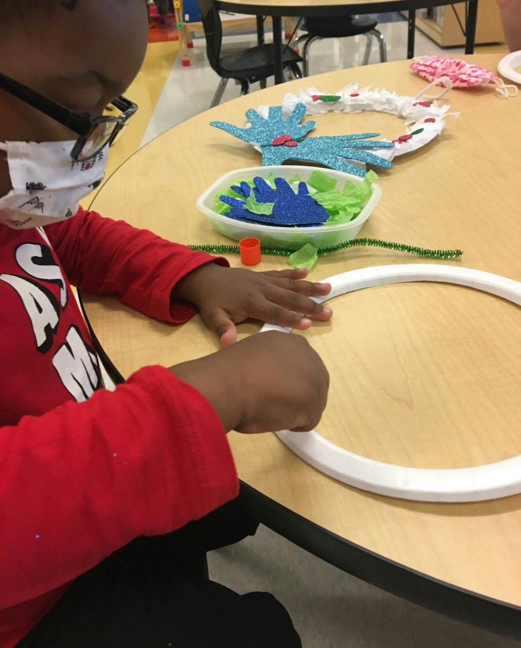 Child in glasses and mask working on a craft project at a table