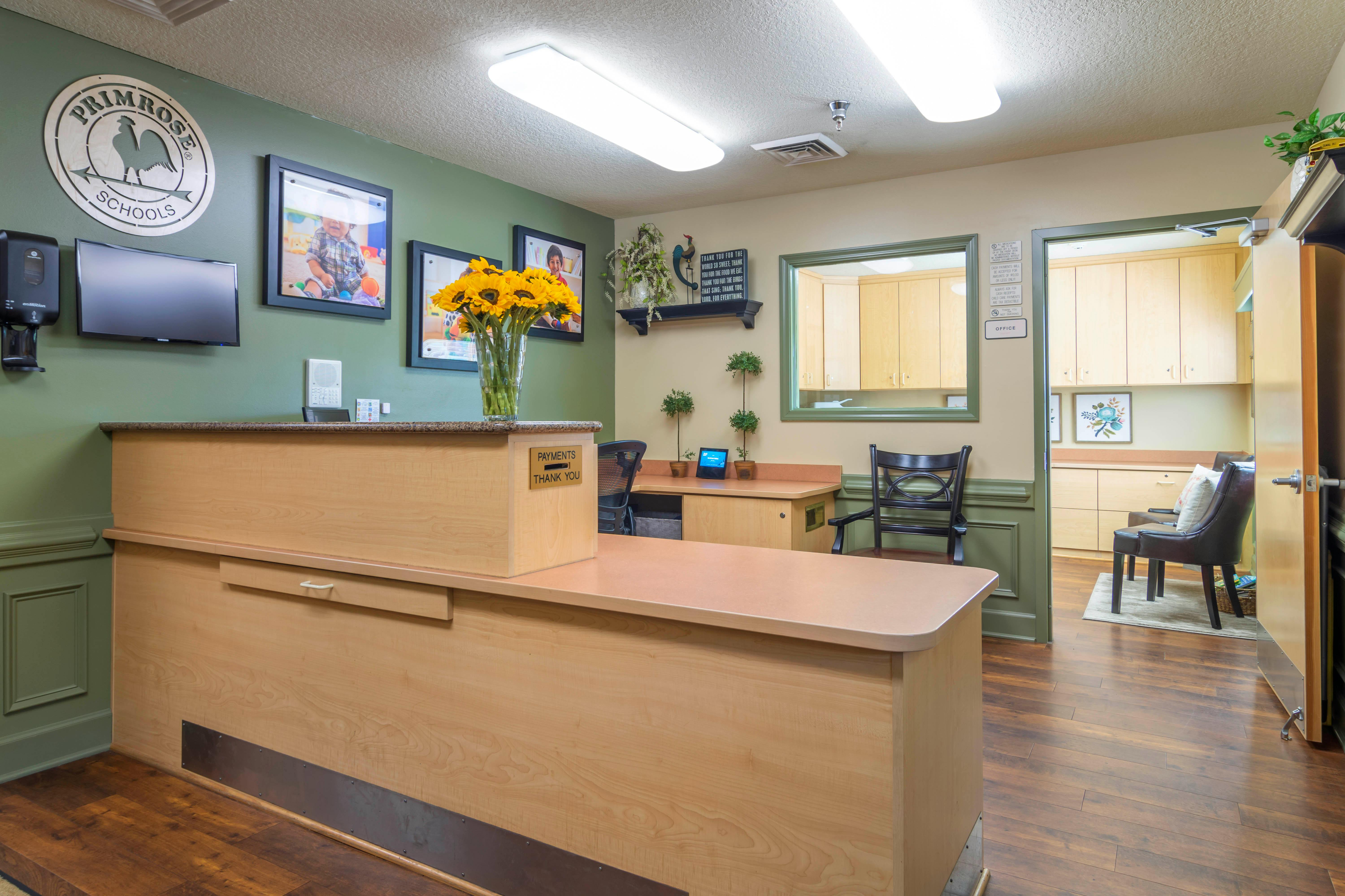 Reception desk with Primrose Schools logo, sunflowers, and office beyond