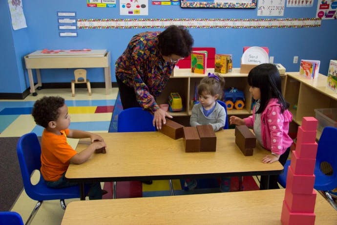 An adult and three children playing with blocks at a table in a classroom