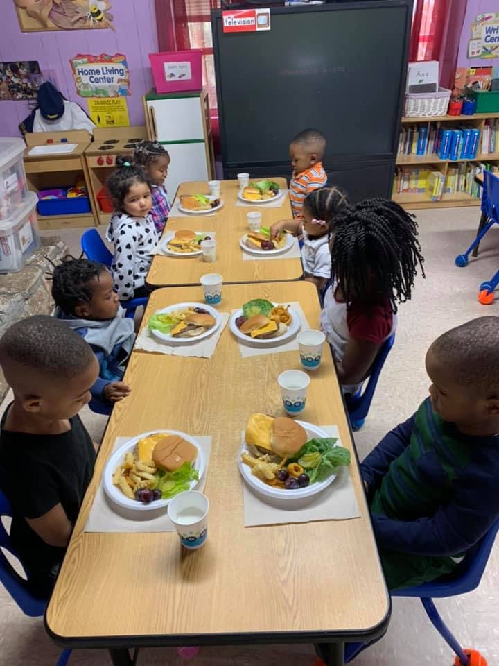 Children sitting at tables with plates of food in a classroom