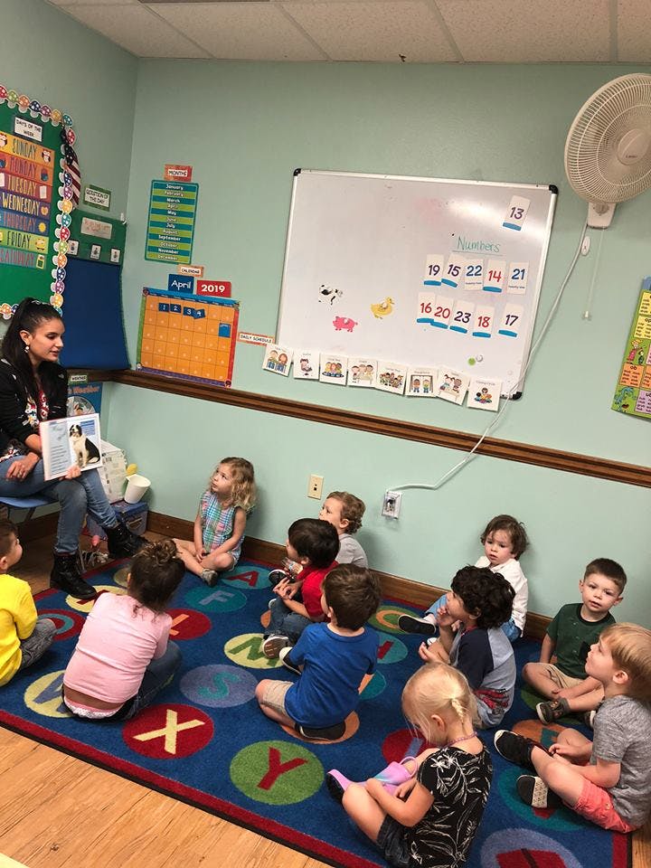 Person reading a book to a group of children in a classroom