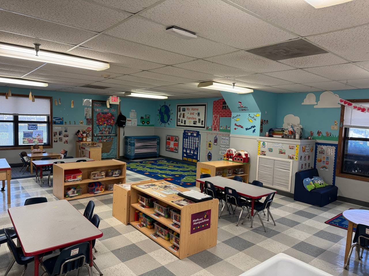 A classroom with small tables and chairs, shelves with toys, and decorated walls