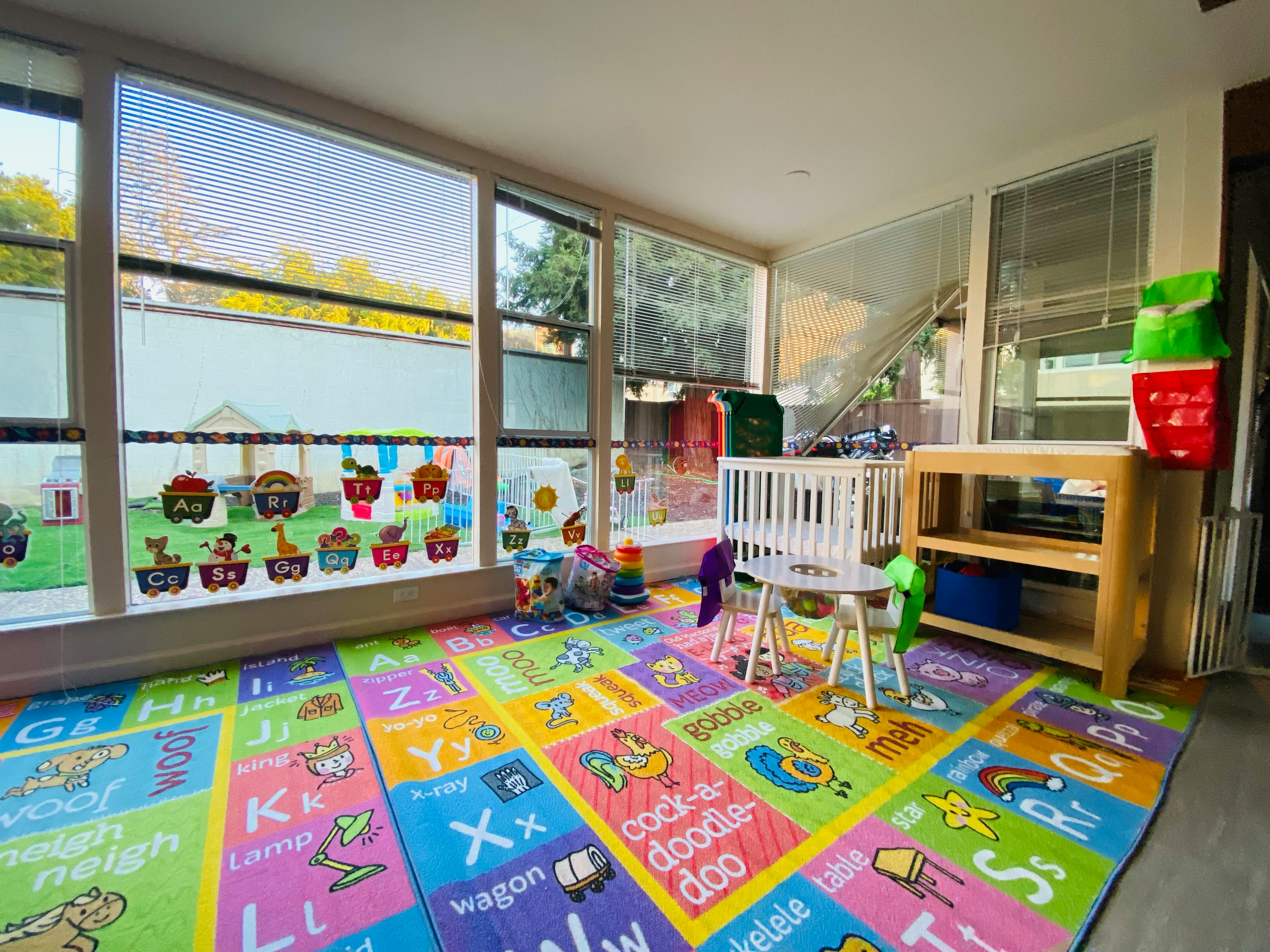 Playroom with alphabet rug, windows, and a small crib