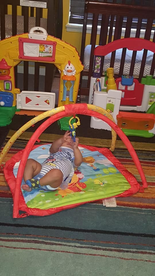Child lying on a play mat under an activity arch, reaching for a toy