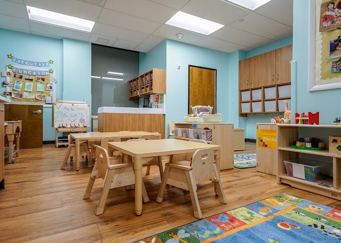 Empty children's classroom with small wooden tables, chairs, and play equipment