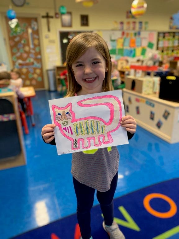 Child holding up a drawing of a cat in a classroom