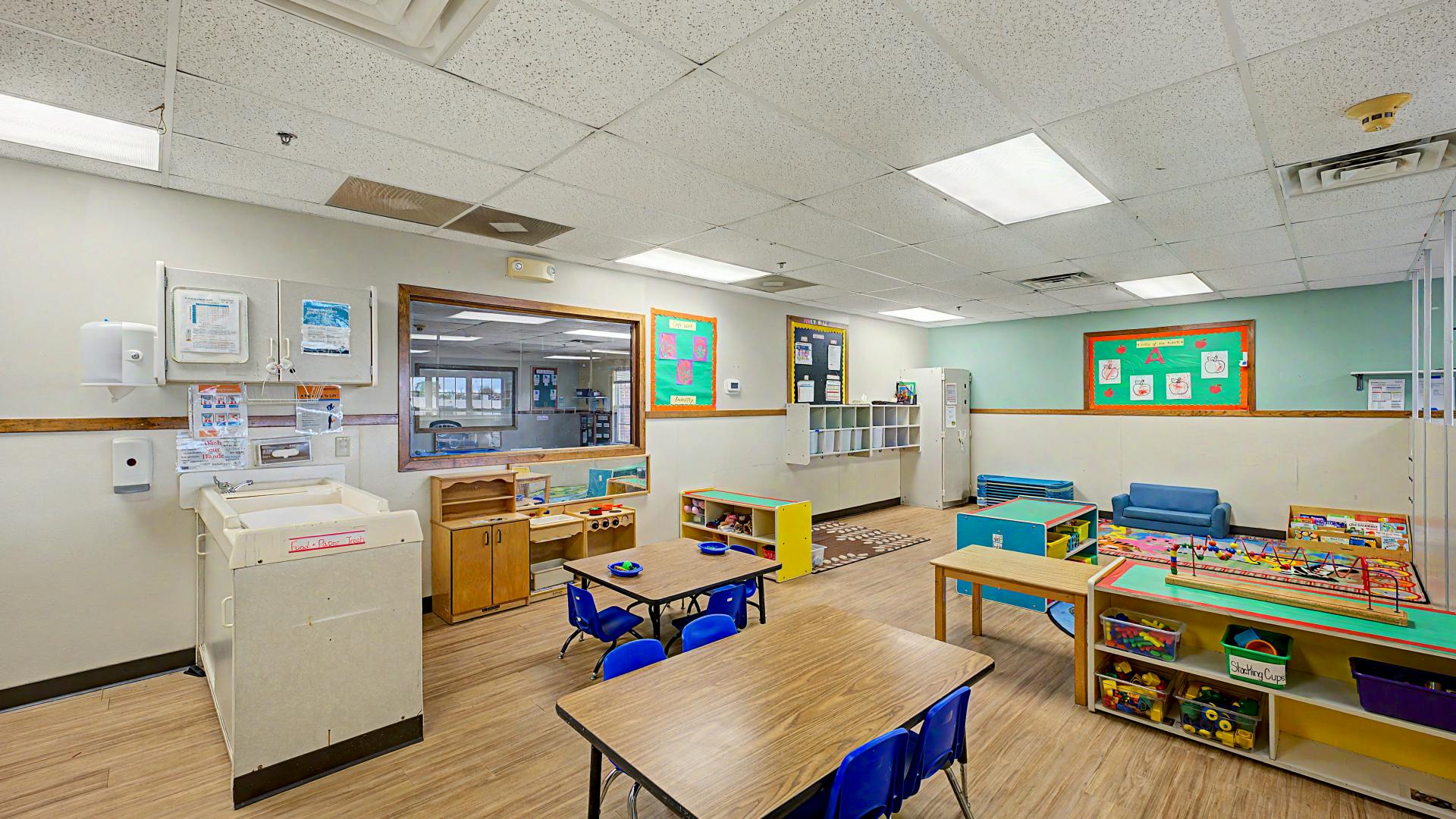 Classroom with child-sized tables and chairs, toys, and bulletin boards