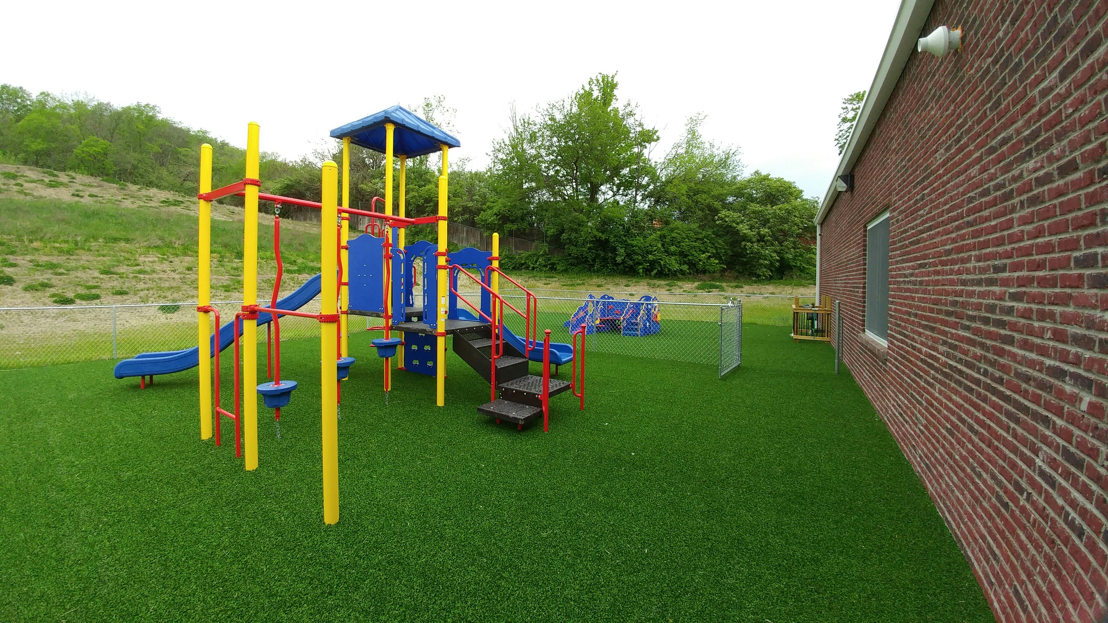 Playground with slides and climbing structures on artificial turf next to a brick building