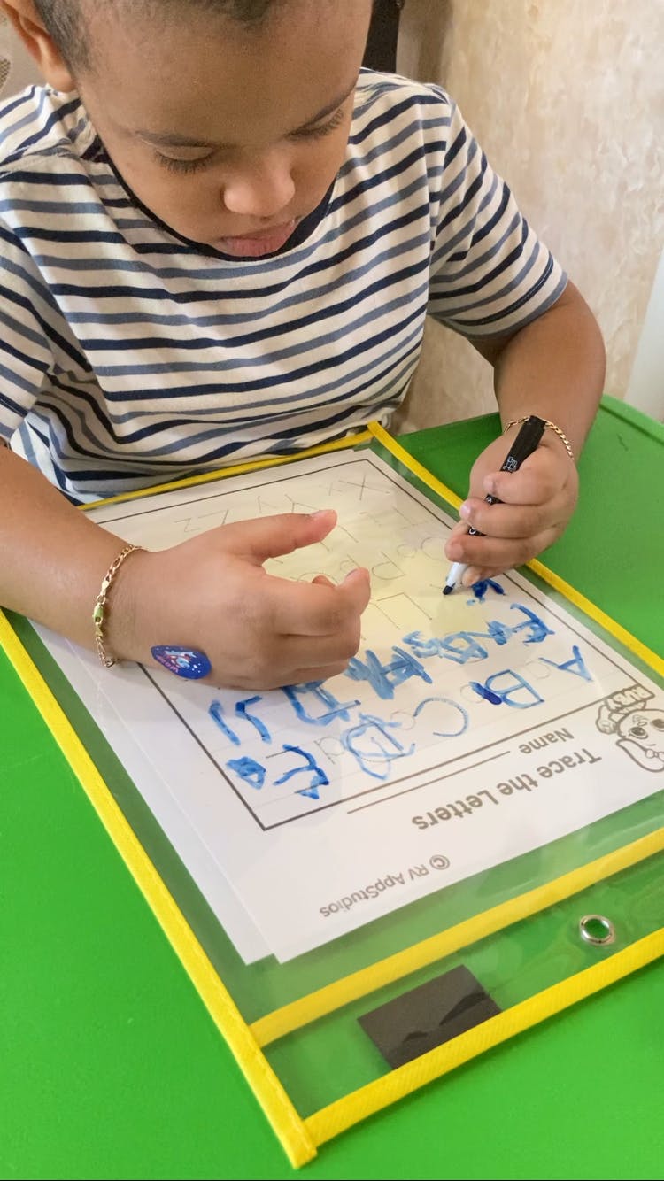 Child tracing letters on a worksheet with a marker