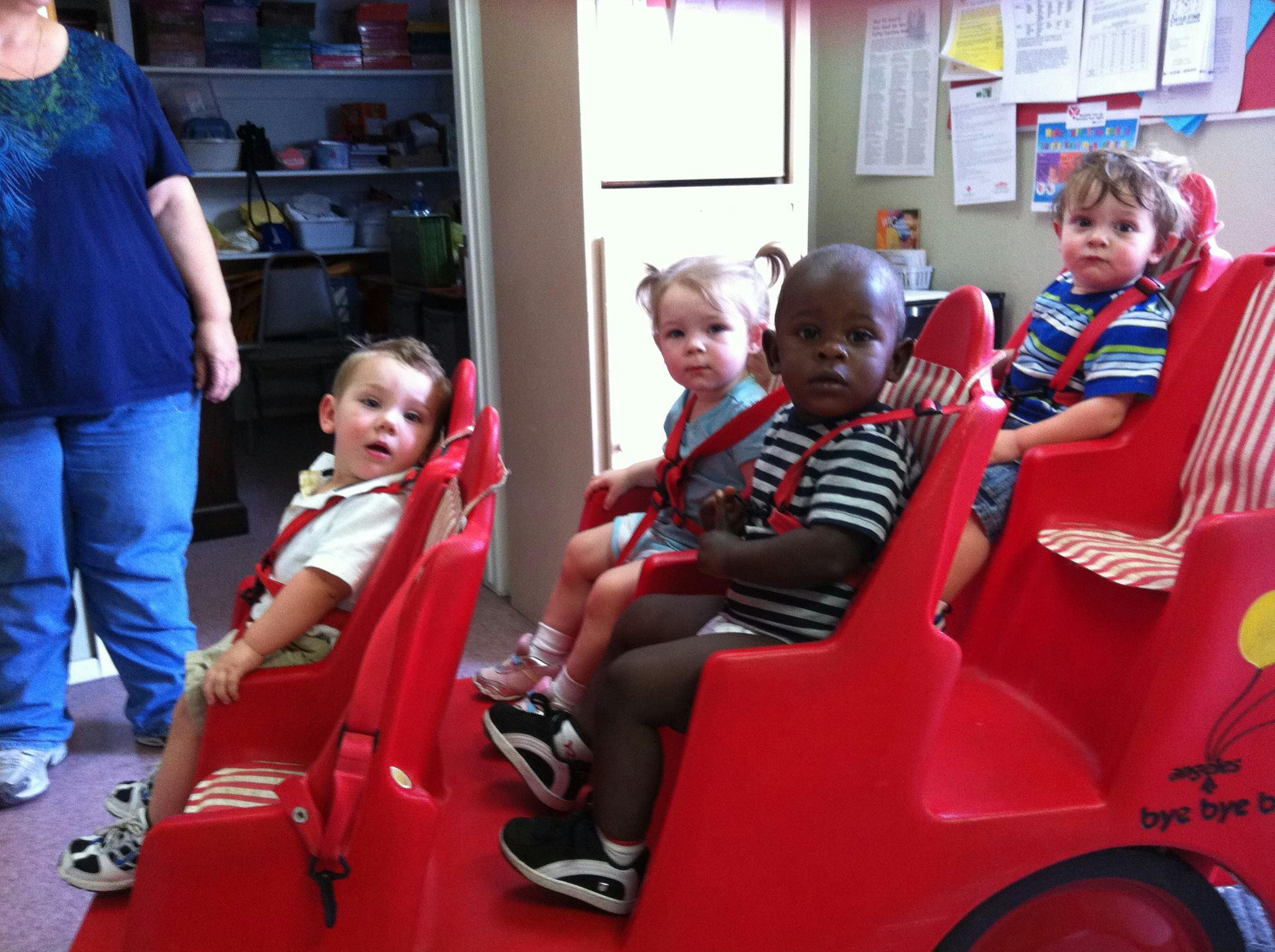 Three children in red seats with a person standing nearby