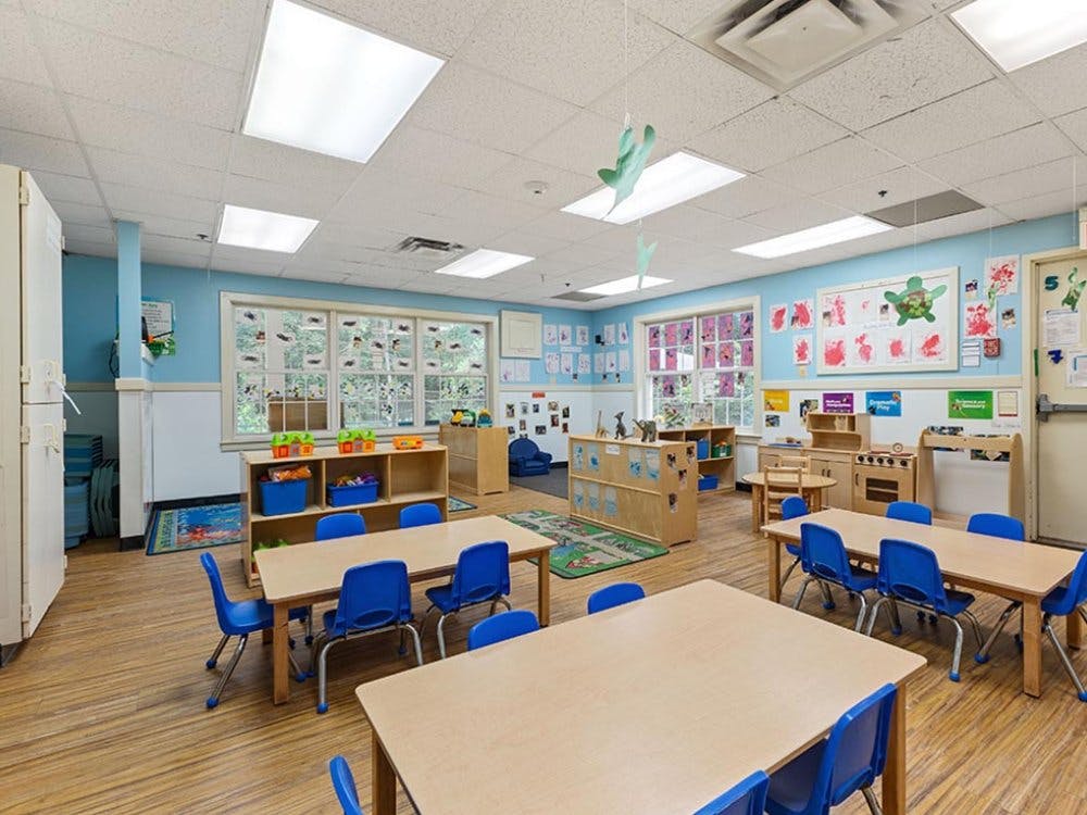 Classroom with small tables and chairs, play kitchen, and windows