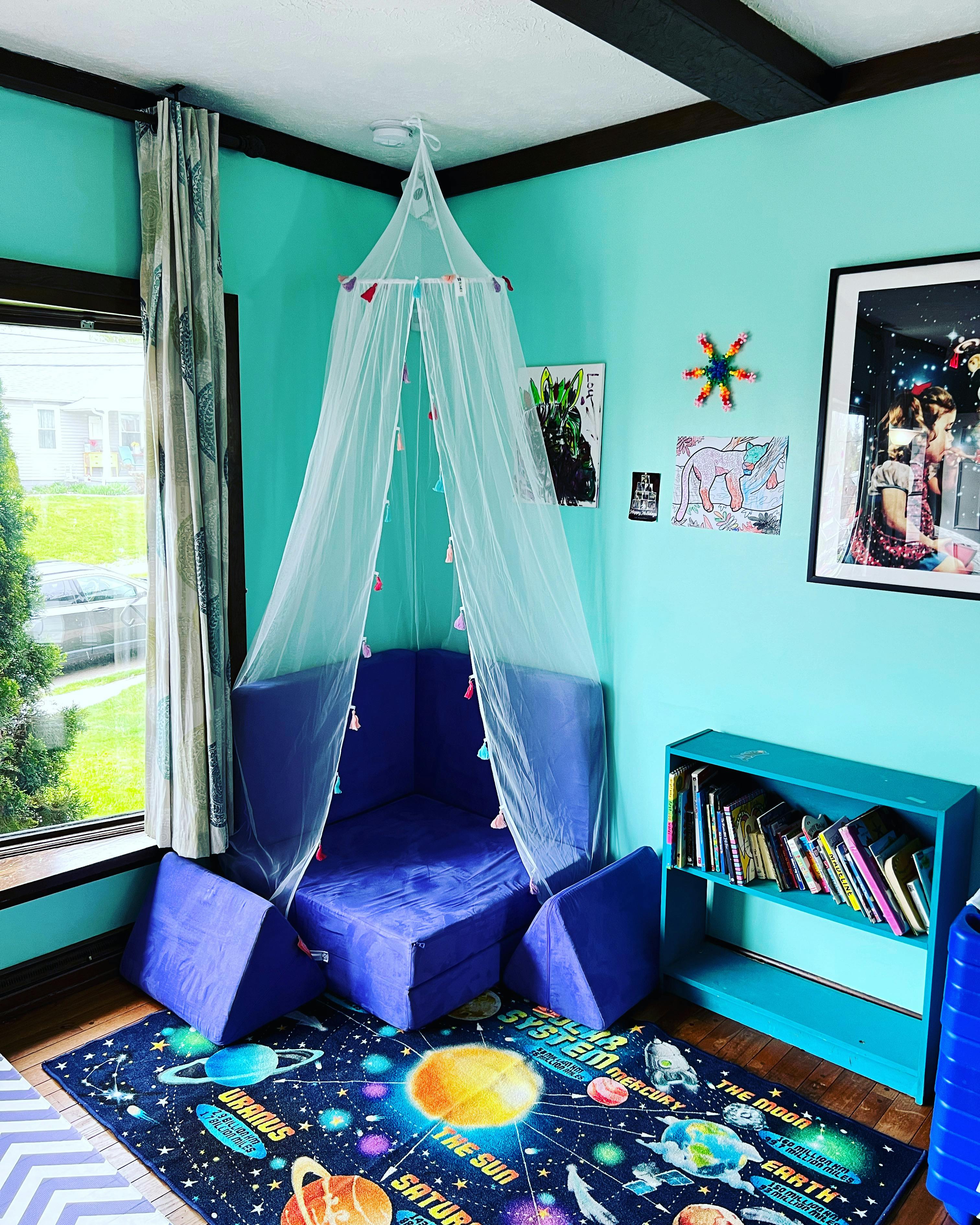Reading nook with blue cushions under a sheer canopy, solar system rug