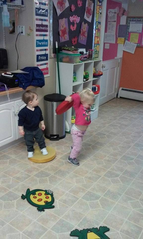 Two children playing in a room, one standing on a yellow disc