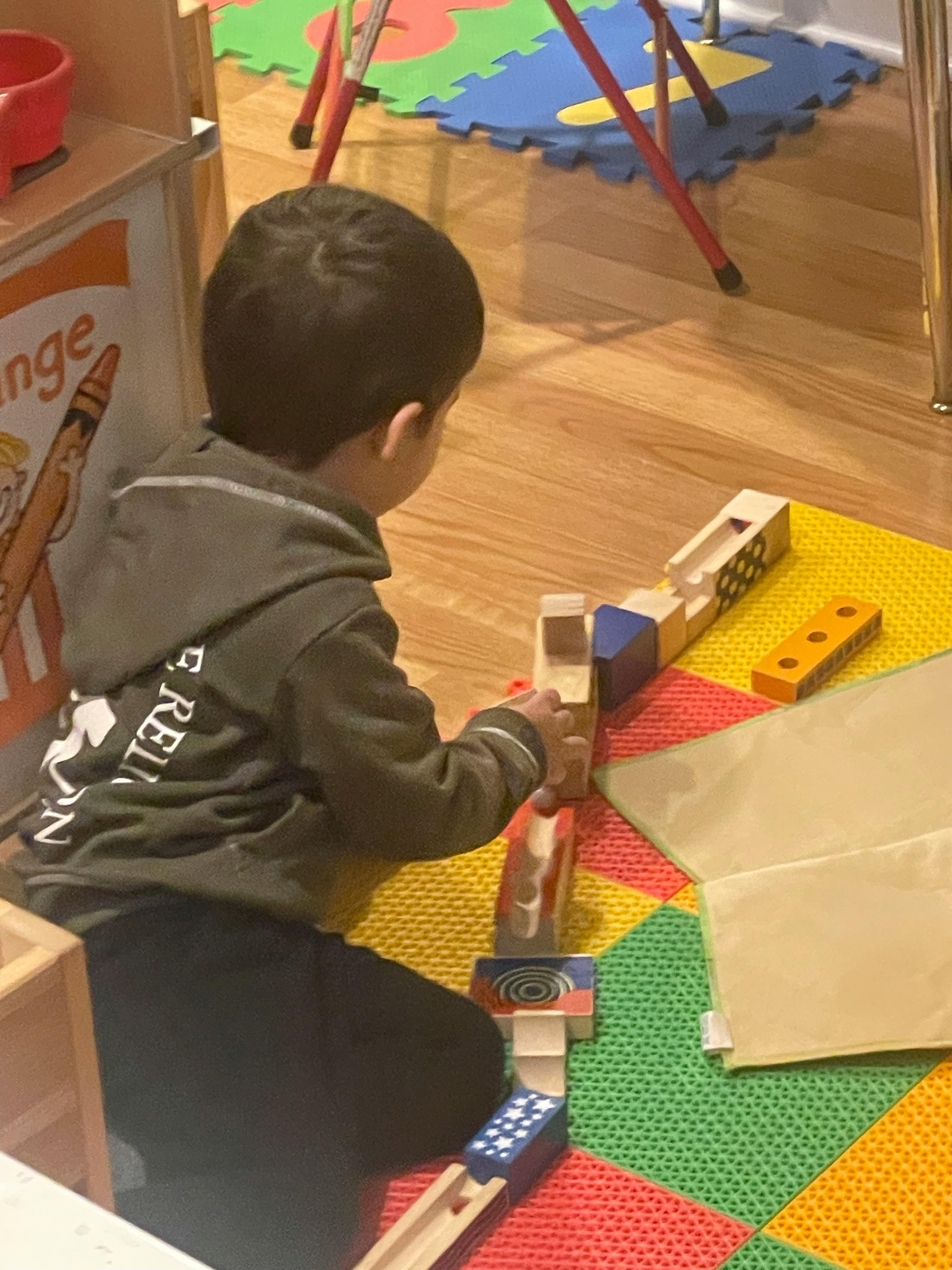 Child playing with a wooden train set on a colorful mat