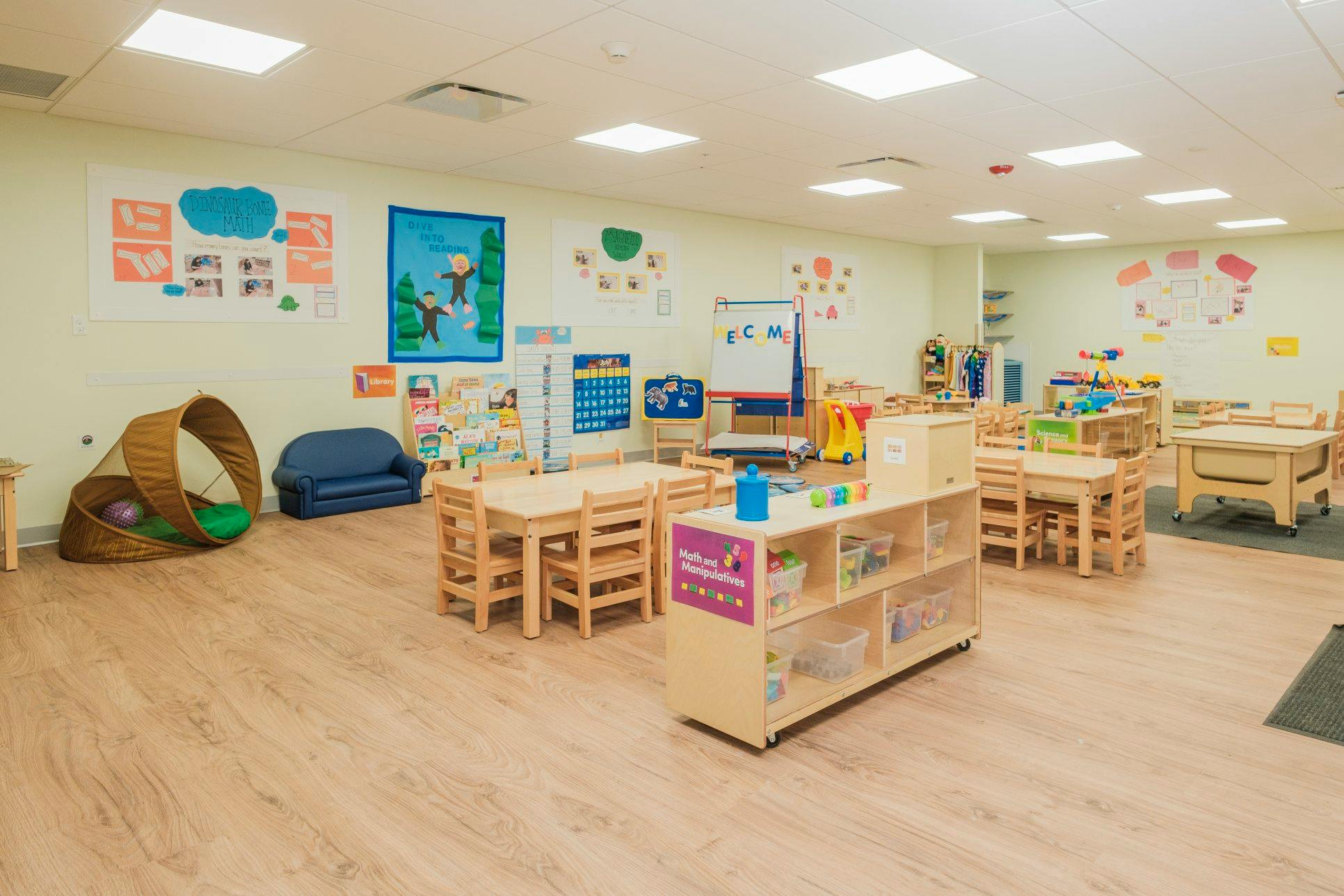 Empty classroom with small tables and chairs, shelves, and educational posters