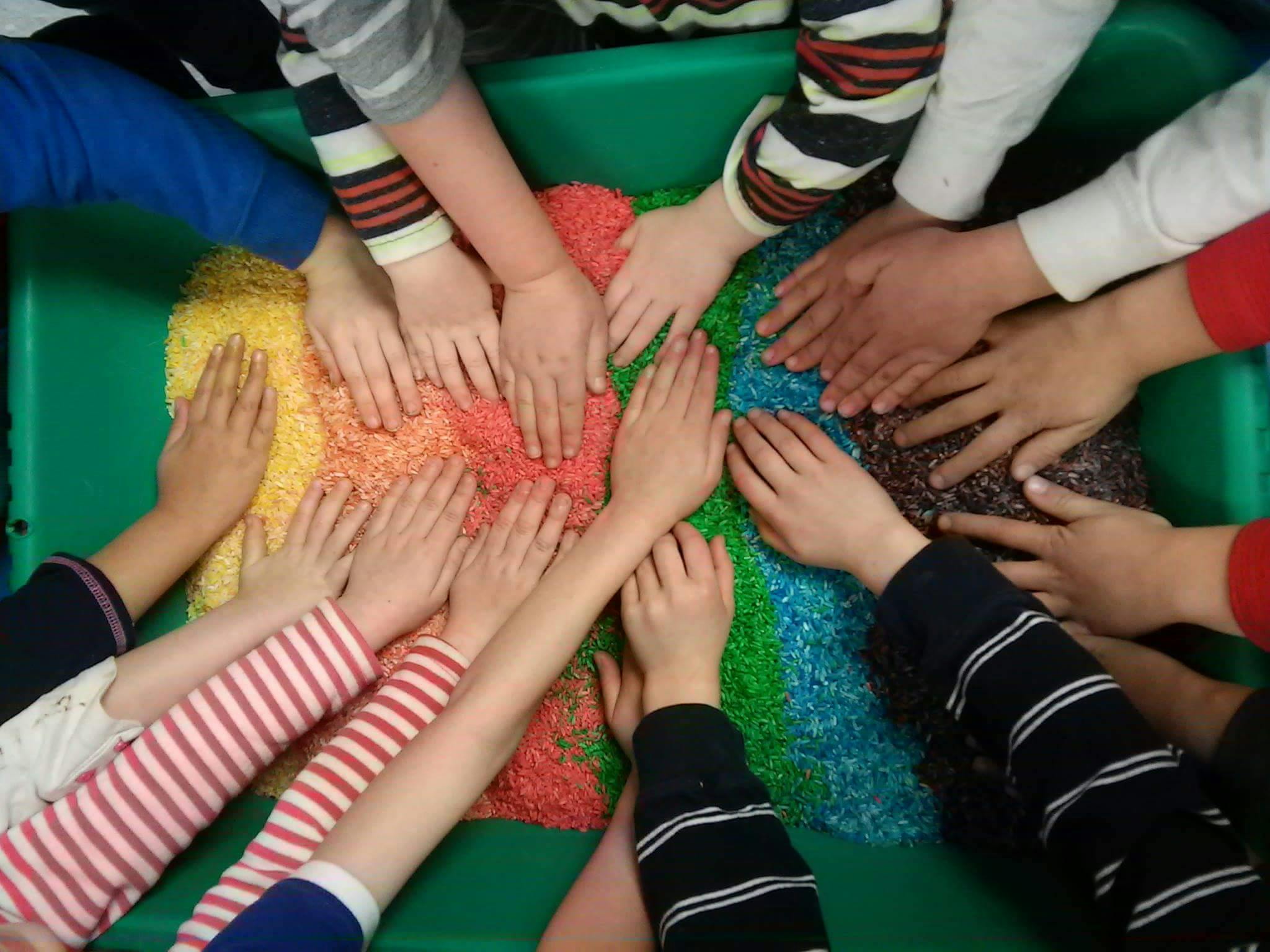 Multiple children's hands touching colorful sensory bin filler