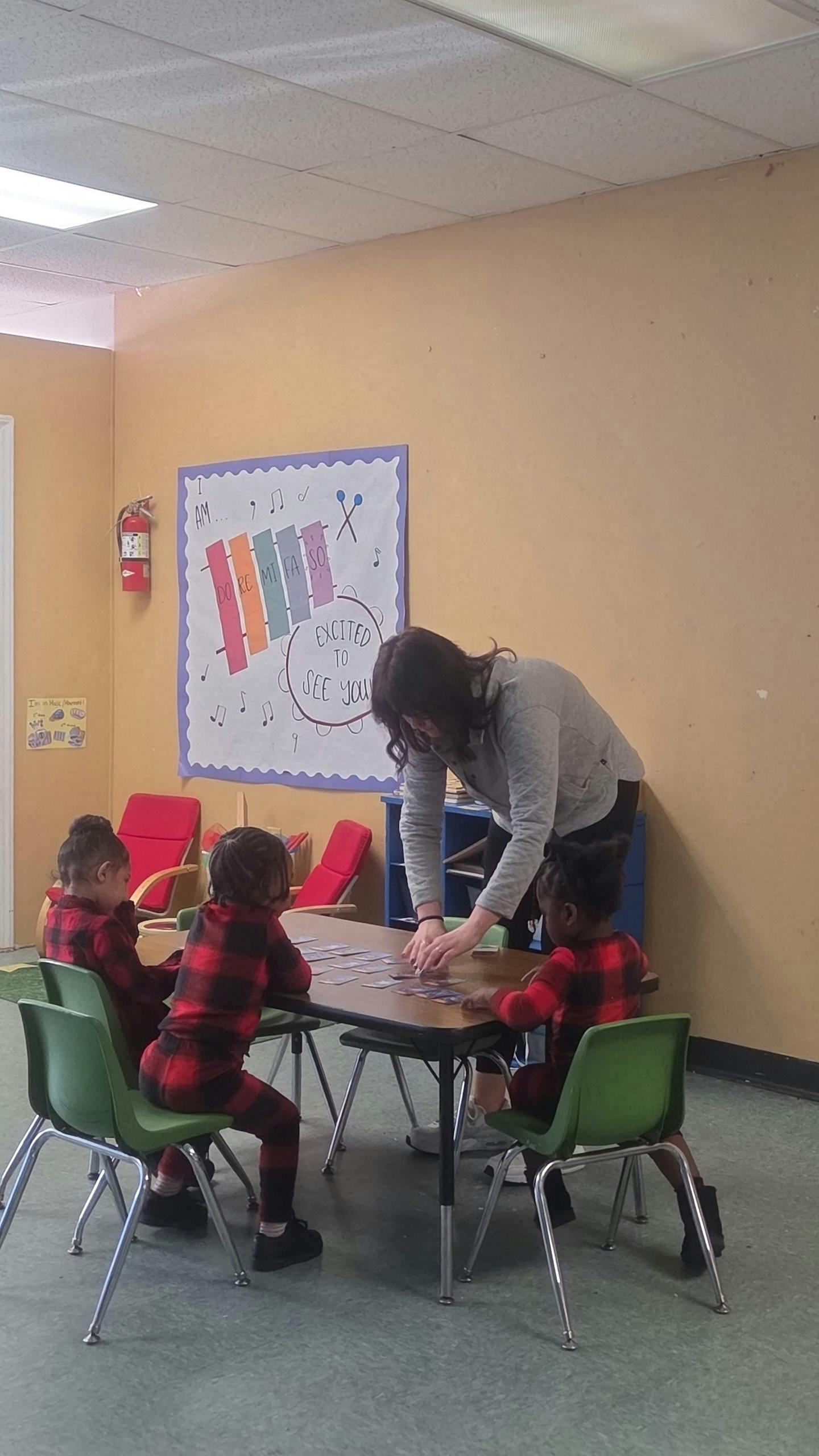Adult helping three children play a card game at a table in a classroom
