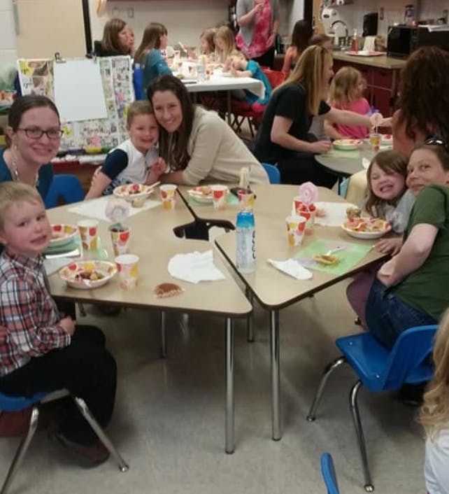 Adults and children sitting at tables with food in a classroom