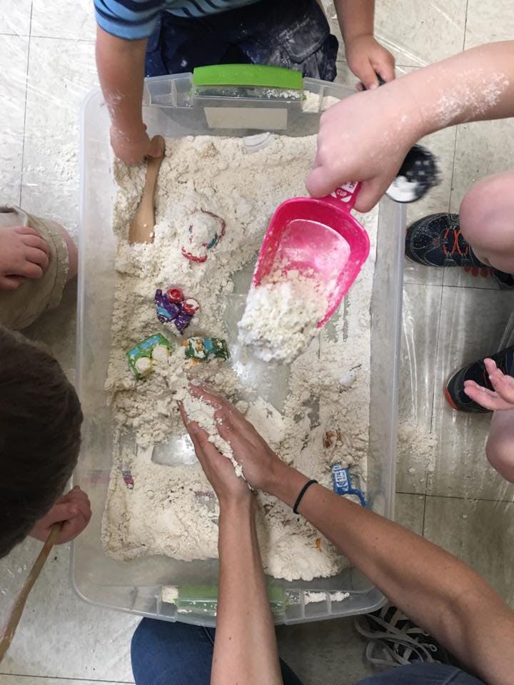 People playing with sand in a clear bin
