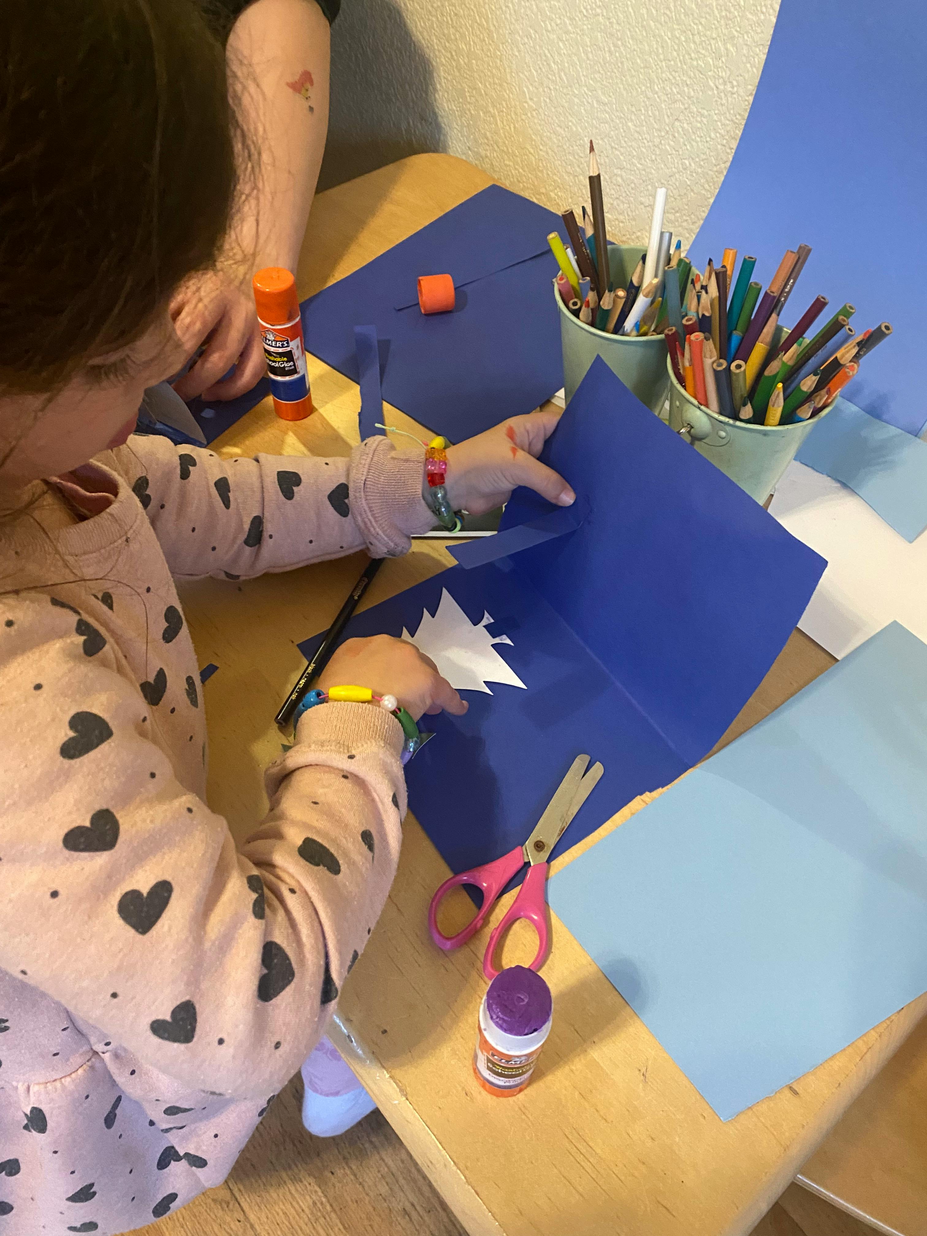 Child making a paper craft with blue paper and white cutouts