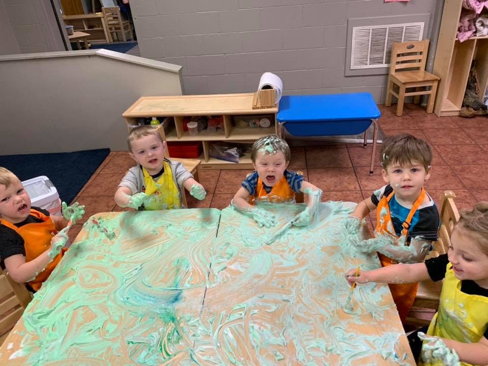 Children playing with green and blue paint on a table