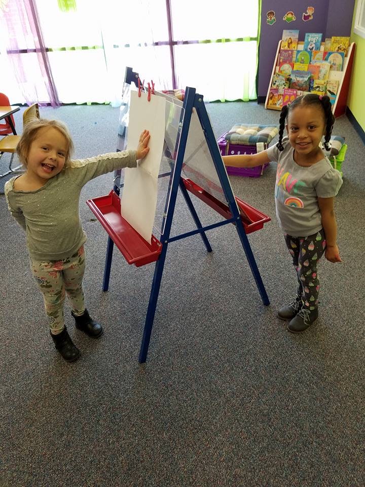 Two children standing on either side of an easel in a classroom