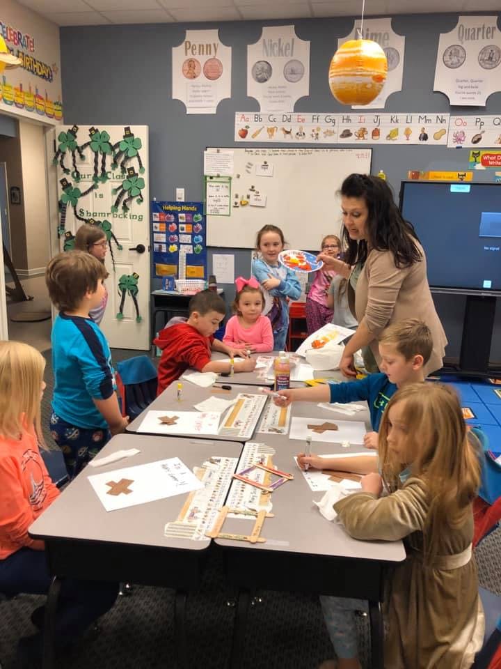 Adult person interacting with children at tables in a classroom