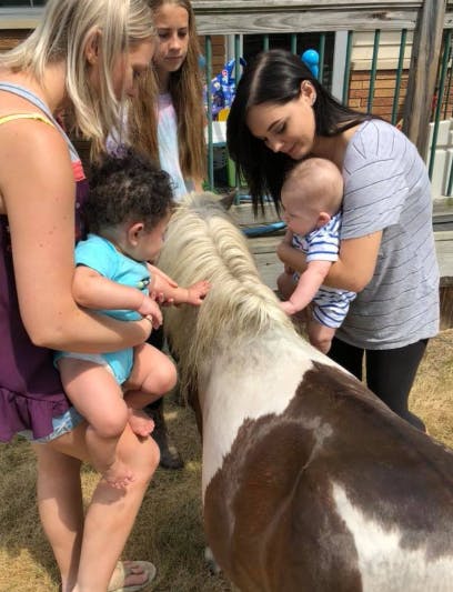 Two people holding babies interacting with a pony