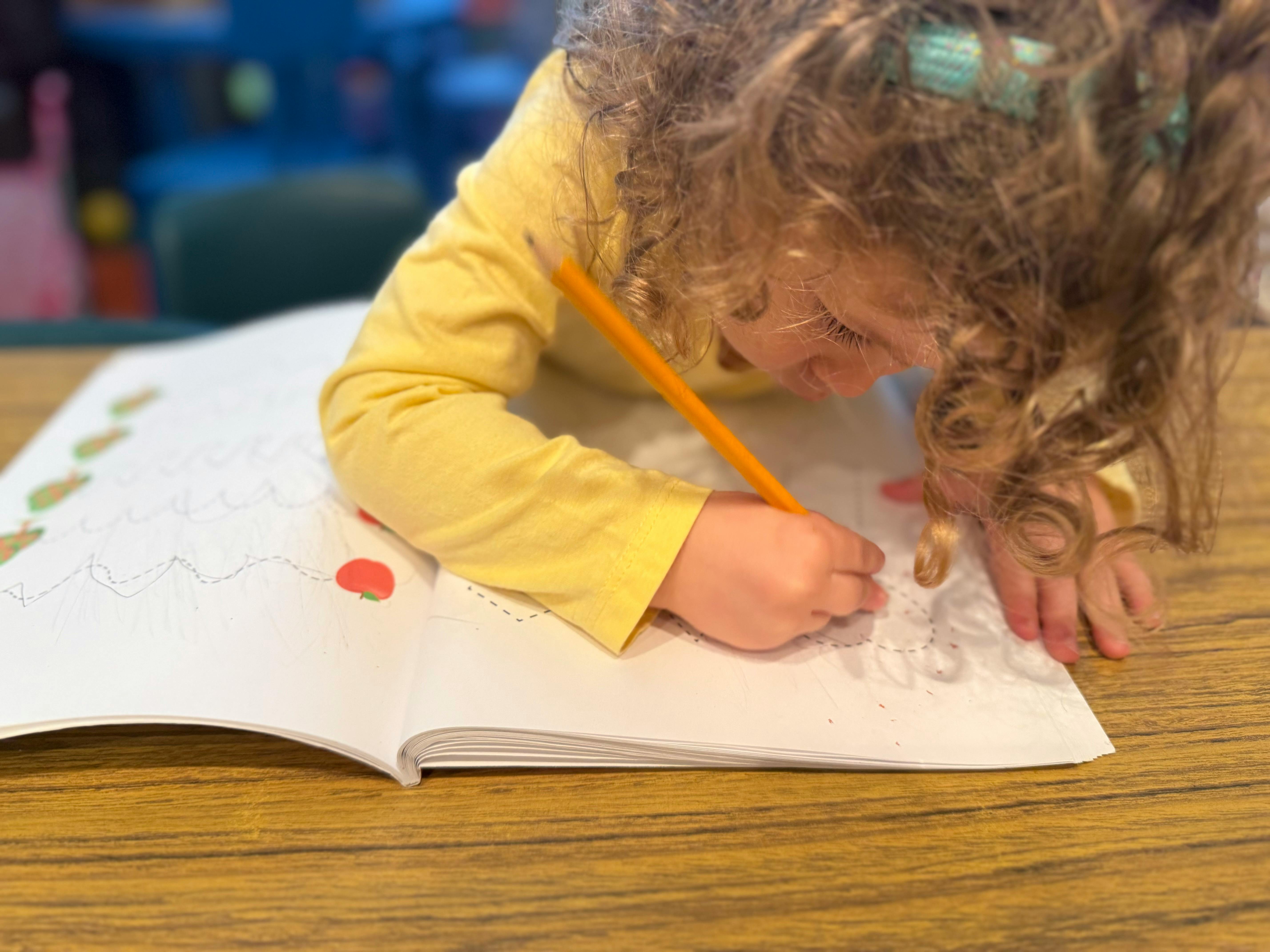 Child drawing in a book with a pencil