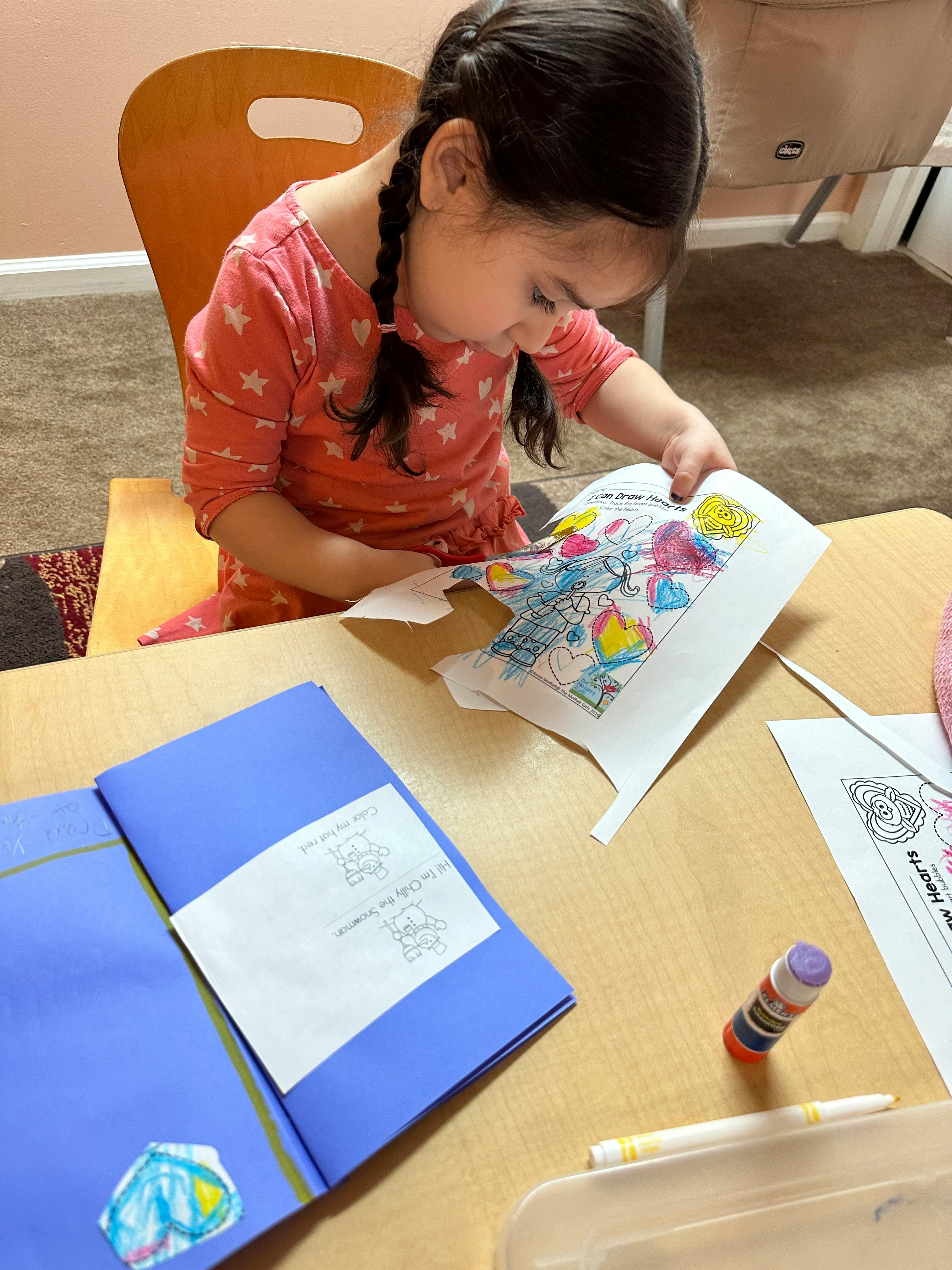 Child cutting out a colorful drawing at a table