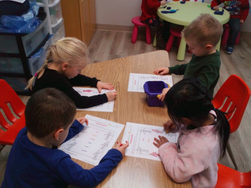 Four children sitting at a table, drawing on papers