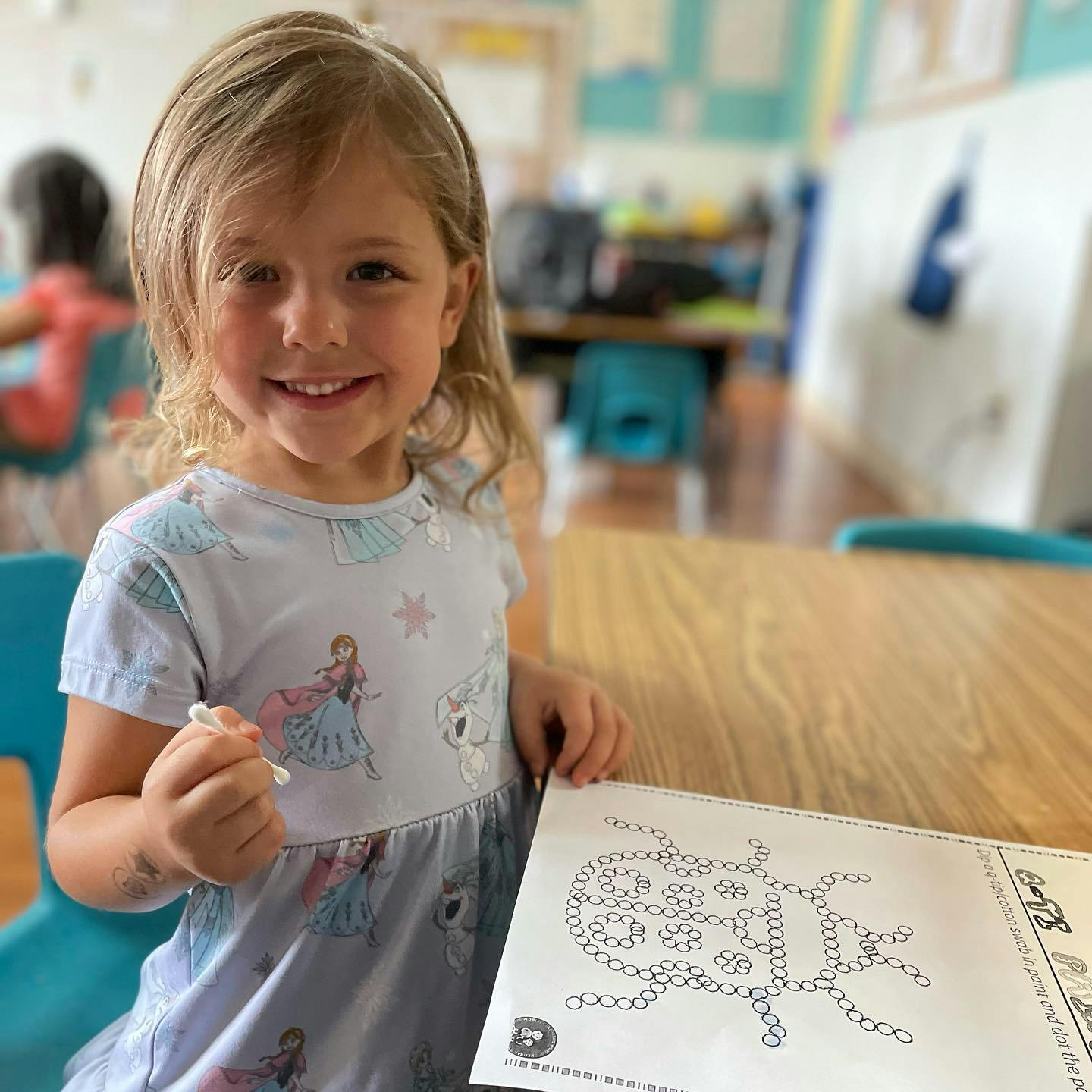 Child holding a small object and looking at a drawing on a table