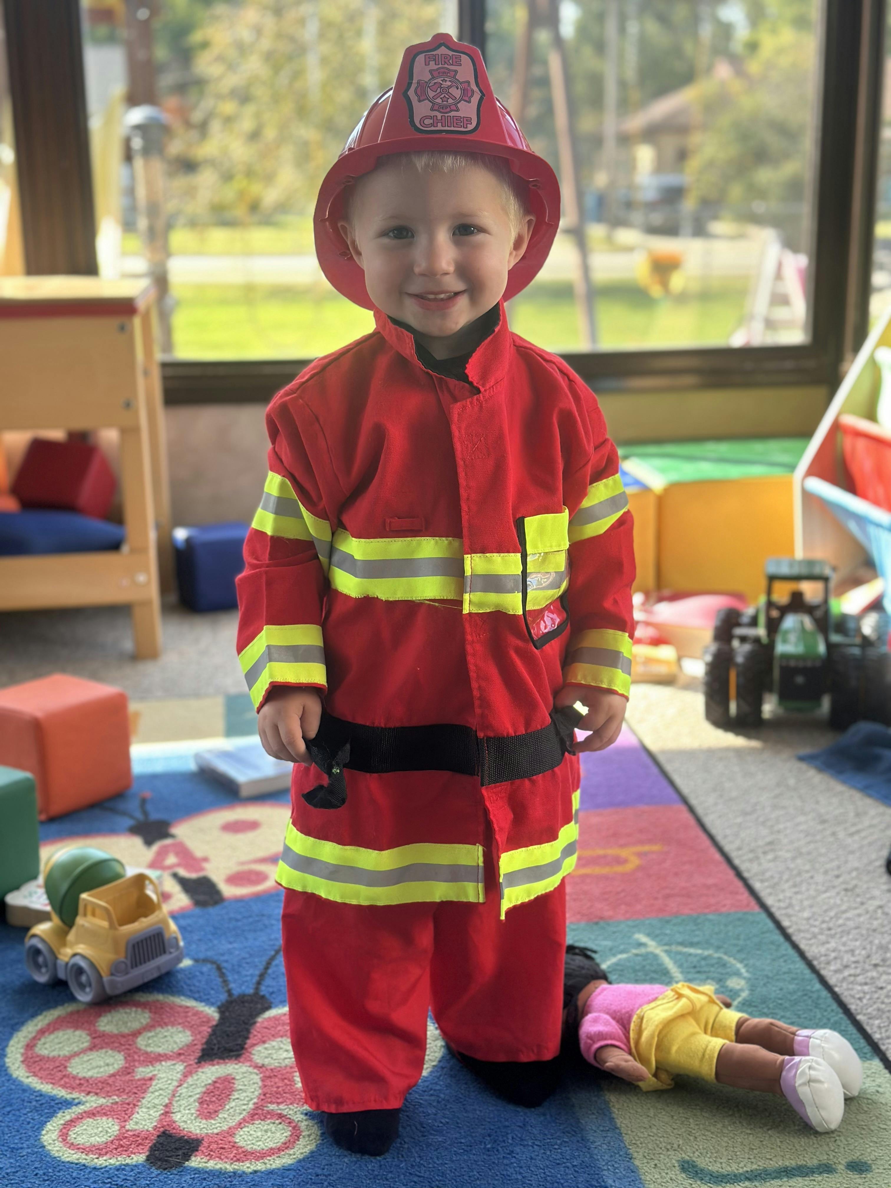 Child in a firefighter costume standing on a colorful rug