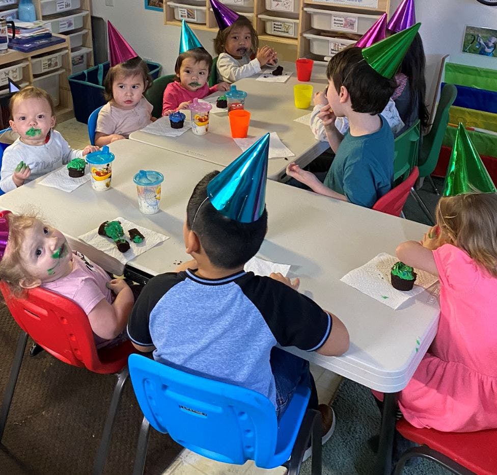 Children wearing party hats sitting at a table with cupcakes